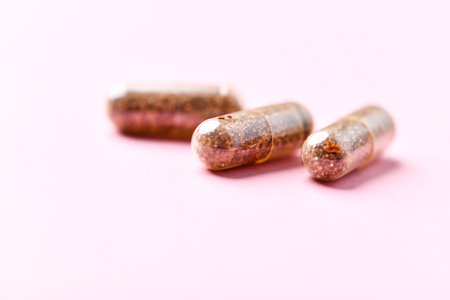 Two golden capsules on a pink background, close-up, macro