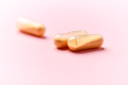 Two golden capsules on pink background. Focus on foreground, soft bokeh.