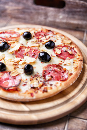 Pizza with salami, olives and cheese on wooden backgroundの写真素材