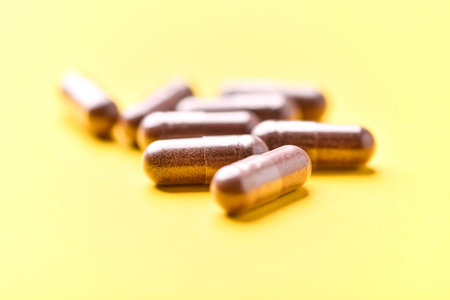Close up of capsule pills on yellow background. Focus on foreground, soft bokeh.