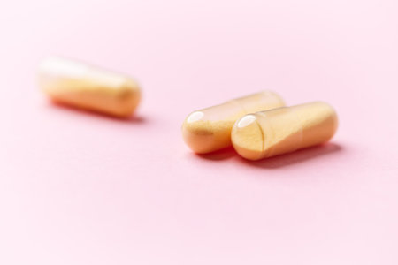 Two yellow capsules on pink background. Focus on foreground, soft bokeh.