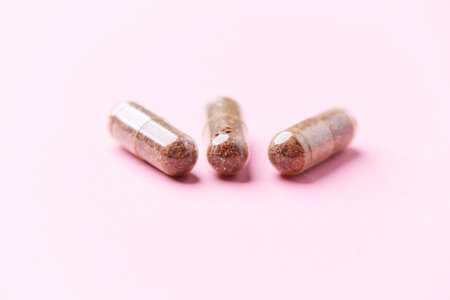 Herbal medicine capsules on pastel pink background. Copyspace.