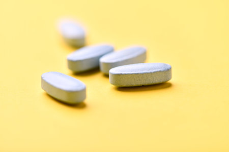 Close up of white pills on yellow background. Focus on foreground, soft bokeh.