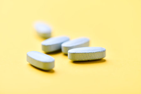Close up of white pills on yellow background. Focus on foreground, soft bokeh.の写真素材