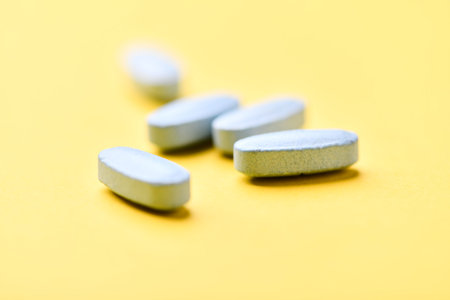Close up of white pills on yellow background. Focus on foreground, soft bokeh.