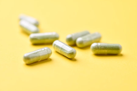 Green capsule pills on yellow background. Focus on foreground, soft bokeh.の写真素材