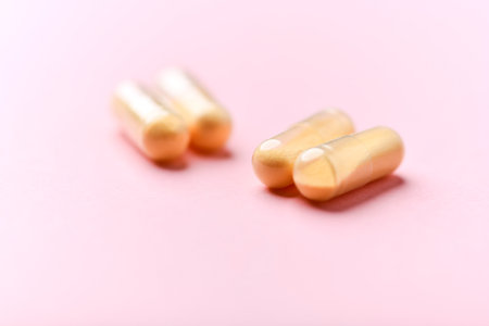 Closeup of golden pills on pink background. Focus on foreground, shallow depth of field.の写真素材