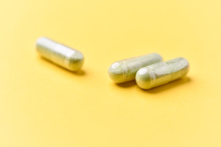 Two green capsules on yellow background. Focus on foreground, soft bokeh.の写真素材