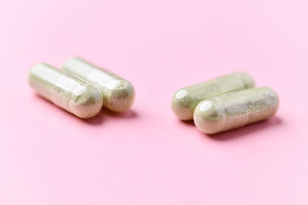 Two capsules of green color on a pink background. Close up.の写真素材