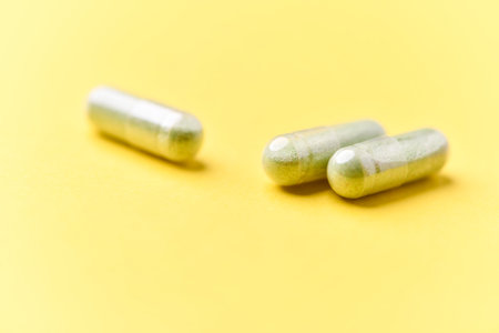 Two green capsules on yellow background. Focus on foreground, soft bokeh.の写真素材