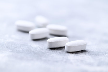 Heap of white pills on gray background. Focus on foreground, soft bokeh.
