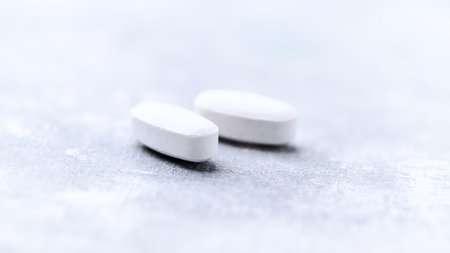 Close-up of two white pills on a gray background. Focus on foreground, soft bokeh.