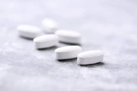 Heap of white pills on gray background. Focus on foreground, shallow DOF.
