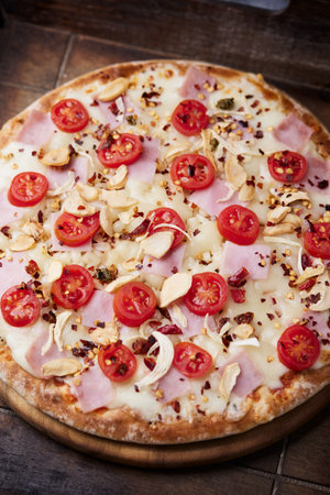 Pizza with ham, cheese, tomatoes and pine nuts on wooden backgroundの写真素材