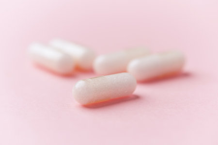 White medical pills on pink background. Focus on foreground, soft bokeh.
