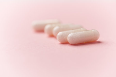 White pills on pink background. Focus on foreground, soft bokeh.