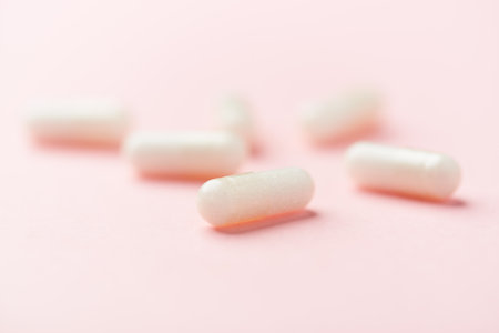 White pills on pink background. Focus on foreground, soft bokeh.