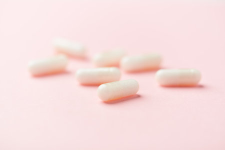 White pills on pink background. Focus on foreground, soft bokeh.