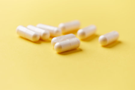 White pills on a yellow background. Focus on foreground, soft bokeh.