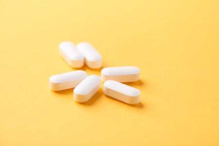 Heap of white pills on yellow background. Focus on foreground.