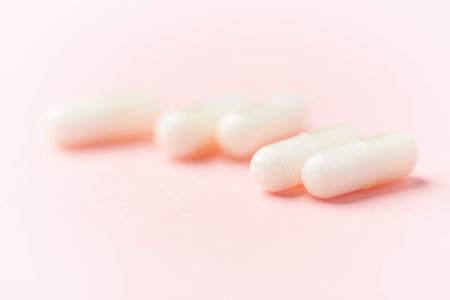 White pills on a pink background. Focus on foreground, soft bokeh.