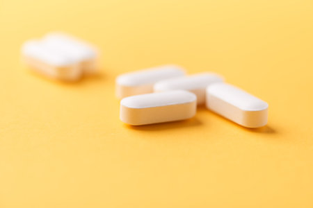 Close up of white pills on yellow background. Focus on foreground, soft bokeh. Pharmacy drug store...