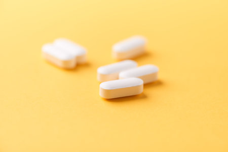 White pills on yellow background. Focus on foreground, soft bokeh.