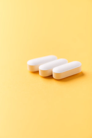 Three white pills on yellow background. Focus on foreground, soft bokeh.の写真素材