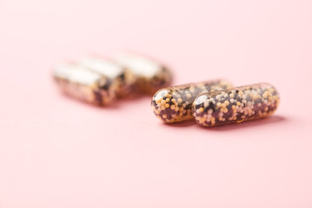 Two capsules with black and white pills on pastel pink background.の写真素材