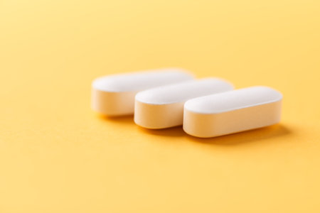 Close up of white pills on yellow background. Focus on foreground, soft bokeh. Pharmacy drug store...