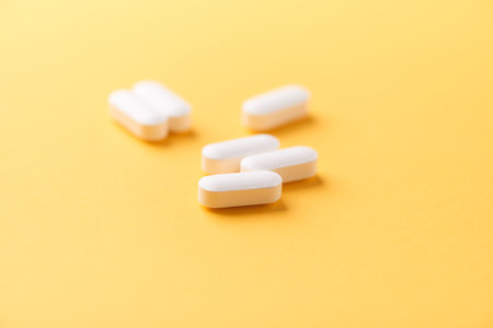 Heap of white pills on yellow background. Focus on foreground.
