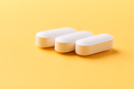 Close up of white pills on yellow background. Focus on foreground, soft bokeh. Pharmacy drug store...