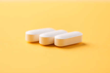Three white pills on yellow background. Focus on foreground, soft bokeh.の写真素材