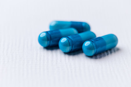 Blue medical capsules on a white background. Focus on foreground, soft bokeh.の写真素材