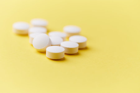 Close up of white pills on yellow background. Focus on foreground, soft bokeh. Pharmacy drugstore...