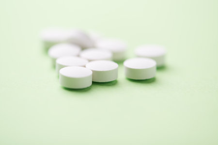 Close up of white pills on green background. Focus on foreground, soft bokeh. Pharmacy drugstore...