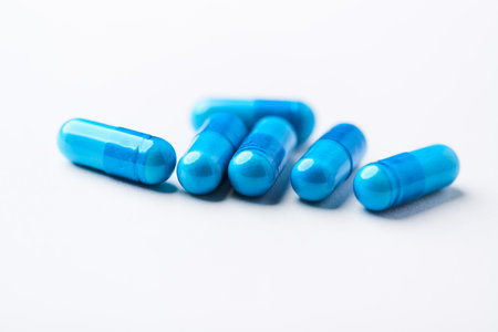 Blue pills on white background. Focus on foreground, soft bokeh.
