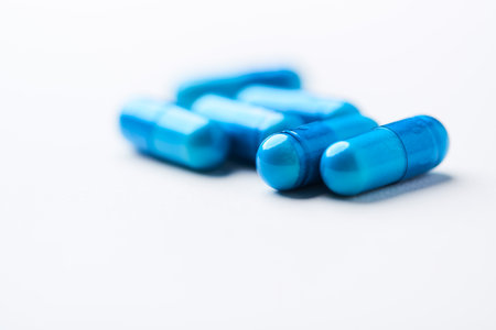 Blue pills on white background. Focus on foreground, soft bokeh.