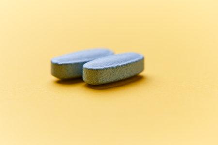 Two blue pills on yellow background. Focus on foreground, soft bokeh.