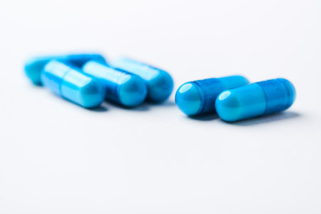 Blue pills on a white background. Focus on foreground, soft bokeh.