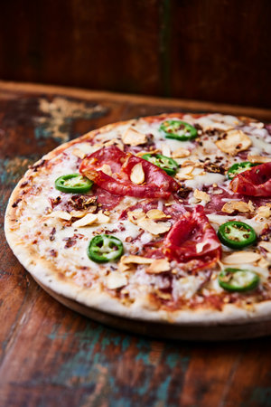 Pizza with salami, jalapeno and pepper on wooden backgroundの写真素材