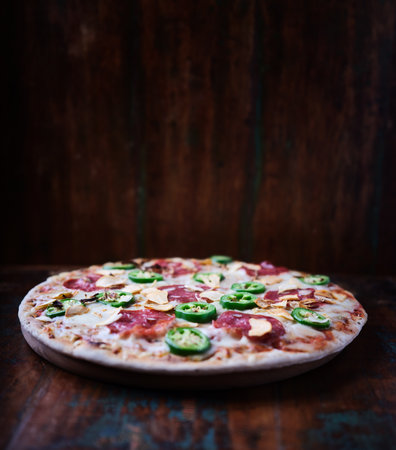 Pizza with salami, pepper and cucumber on wooden backgroundの写真素材