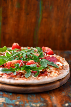 Pizza with salami, arugula and tomatoes on wooden backgroundの写真素材