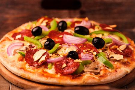 Pizza with salami, olives, pepper and onion on wooden backgroundの写真素材