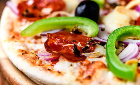 Pizza with sausages and vegetables on a wooden background.