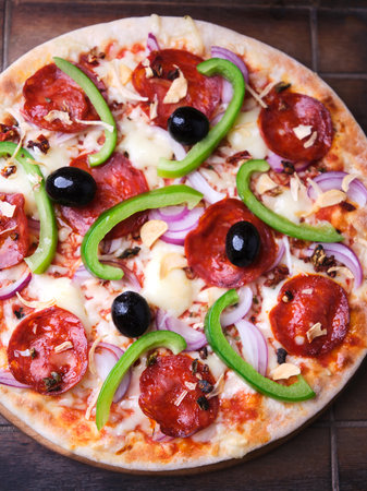Pizza with salami, pepper and olives on wooden backgroundの写真素材