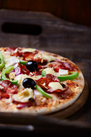 Pizza with salami, pepper, cheese and olives on wooden backgroundの写真素材