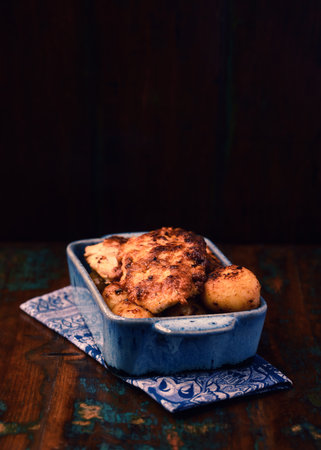 Fried chicken fillet with potatoes in a blue ceramic bowl on a wooden backgroundの写真素材