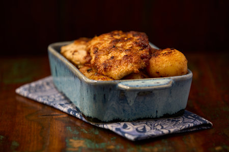 Fried chicken fillet with potatoes in a blue ceramic bowl on a wooden backgroundの写真素材
