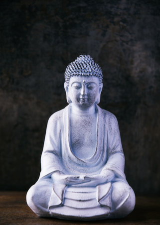 Buddha statue on wooden table in front of dark background.の写真素材